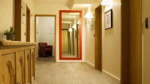 A hotel corridor with wooden flooring, a mirror on the wall, and a red-framed door at the end. - Reinhardts Garni Automobilia Hotel  (Bietigheim-Bissingen)