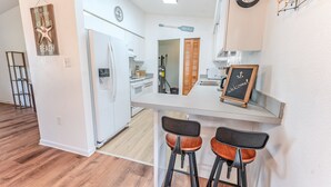 A modern kitchen with a white refrigerator, wooden stools, and a welcome sign. - Charming 2BR Home w/Heated Pool & Arcade in Quiet Area – Perfect Location! (Port Charlotte)