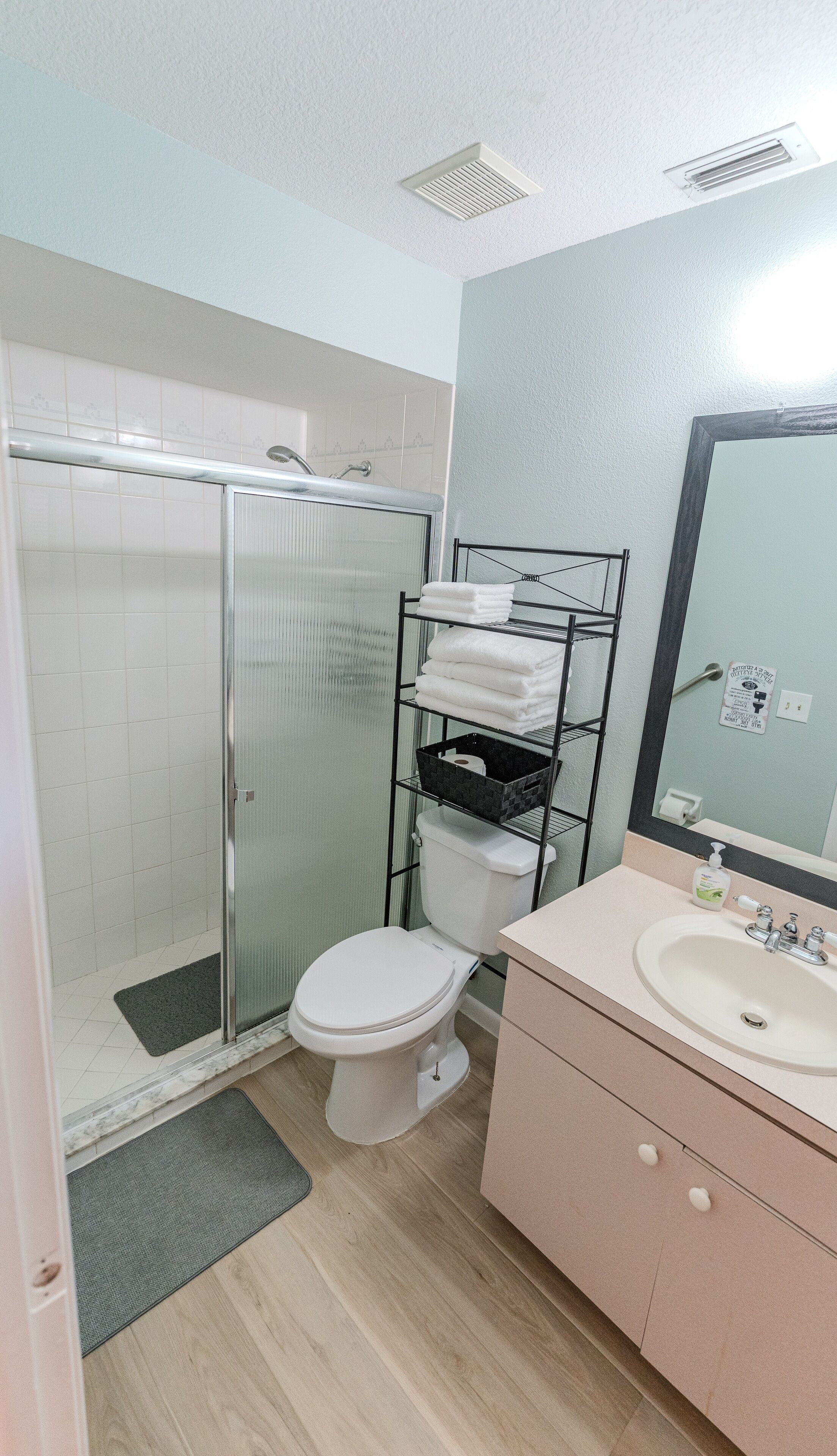 A bathroom with a shower, toilet, sink, and a towel rack.