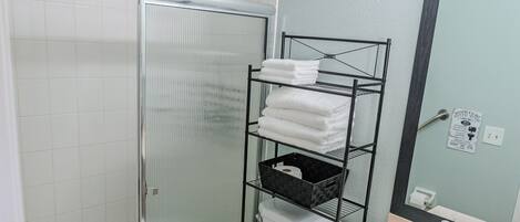 A bathroom with a shower, toilet, sink, and a towel rack.