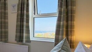 A bedroom with a window overlooking a coastal view, a radiator, and a bed with pillows.