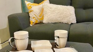 Ein modernes Wohnzimmer mit einem grauen Sofa, einer flauschigen weißen Decke und einem Tablett mit weißen Tassen und Tellern.