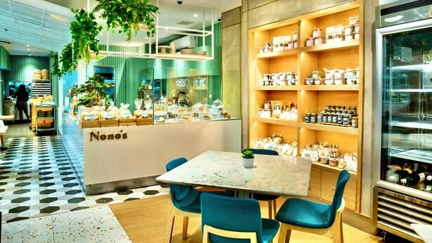 Ein modernes Café-Interieur mit einem zentralen Tisch, blauen Stühlen und Regalen voller Gläser und Behälter.