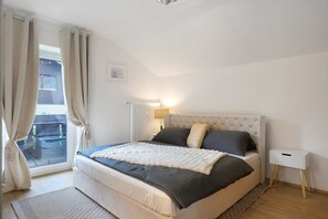 Un dormitorio con cama, mesita de noche, ventana con cortinas y radiador.