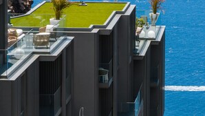 A modern high-rise building with a rooftop garden, glass balconies, and a view of the sea. - Calheta Hills I – With pool and sea view (Calheta)