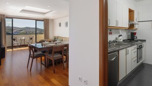 A modern apartment with a dining area, kitchen, and large windows offering a view of the city. - Lobos Horizon – Coziness with Madeiran Soul (Câmara de Lobos)