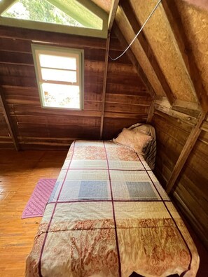 A small, wooden cabin with a sloped ceiling, a single bed with a patterned bedspread, a window, and a wooden floor. - Comfort of nature (Aguas mornas)
