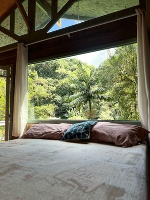 A bed with a view of lush greenery through a window. - Comfort of nature (Aguas mornas)