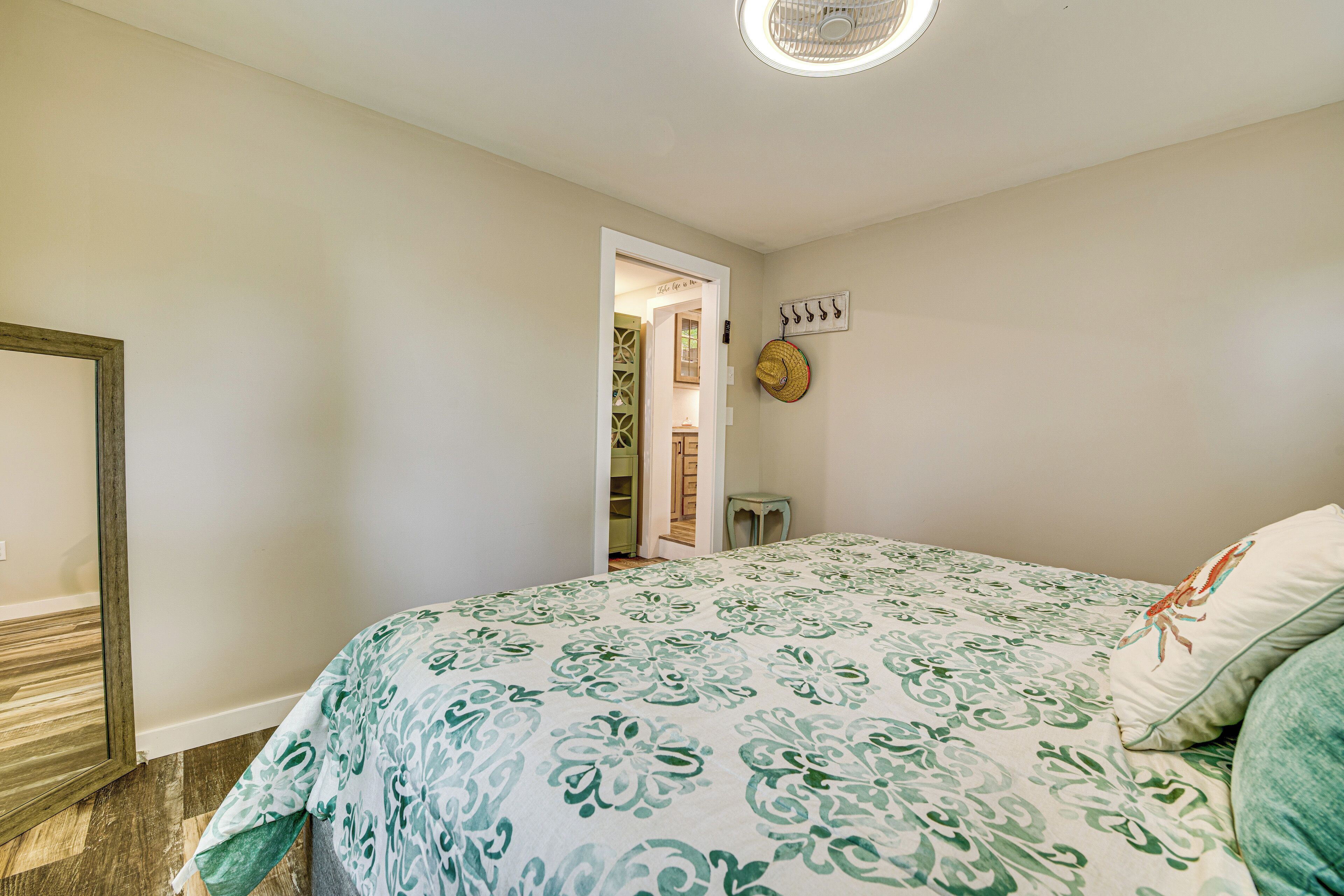 Een slaapkamer met een bed, een deur die naar een andere kamer leidt, en een klein tafeltje met een hoed aan de muur.
