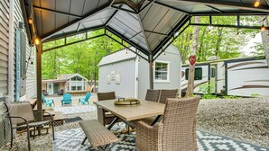 An outdoor patio with a table and chairs, surrounded by a covered area with a view of a house and a trailer. - Lakehouse with Sandy Beach and Boating (Belmont)