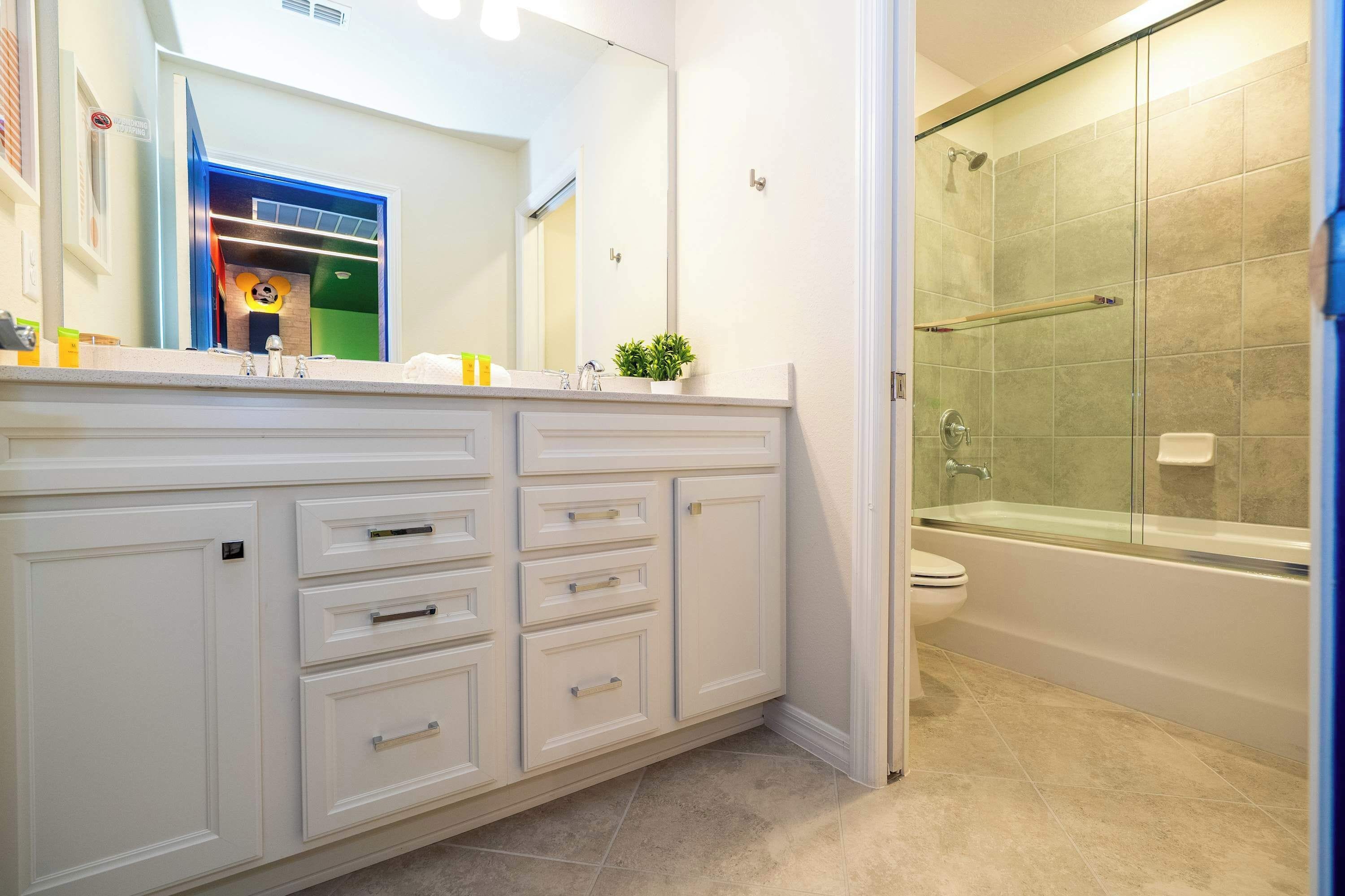A bathroom with a large mirror, a glass shower enclosure, and a white vanity with drawers.