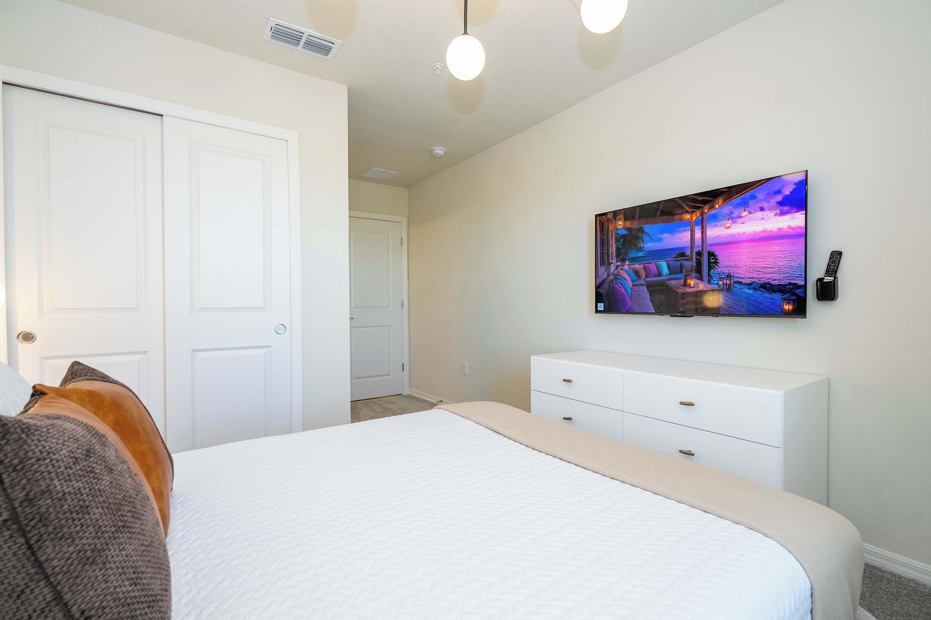 Un dormitorio con una cama, un tocador blanco, un cuadro de una playa y un termostato instalado en la pared.