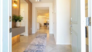 A hallway with a wooden accent wall, a potted plant, a blue and white rug, and a kitchen area in the background. - Family 5Bd Close To Disney At Windsor Cay 16136 (Clermont)