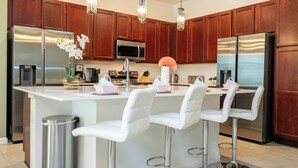 A modern kitchen with stainless steel appliances, wooden cabinets, and white bar stools. - Family Friendly 12Bd W Jacuzzi Veranda Palms 4401 (Kissimmee)