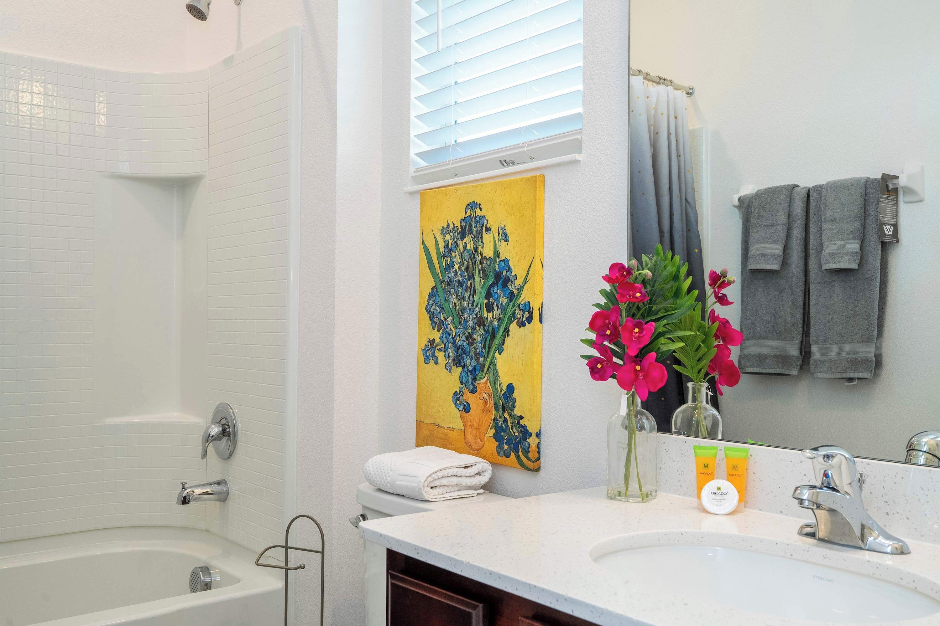 A bathroom with a bathtub, a sink, a mirror, a towel rack, and a painting on the wall.