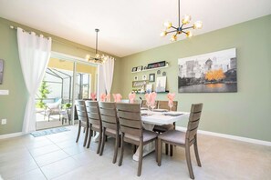 A dining area with a table set for six, surrounded by six chairs, a chandelier, and a cityscape painting on the wall. - Family Friendly 12Bd W Jacuzzi Veranda Palms 4401 (Kissimmee)