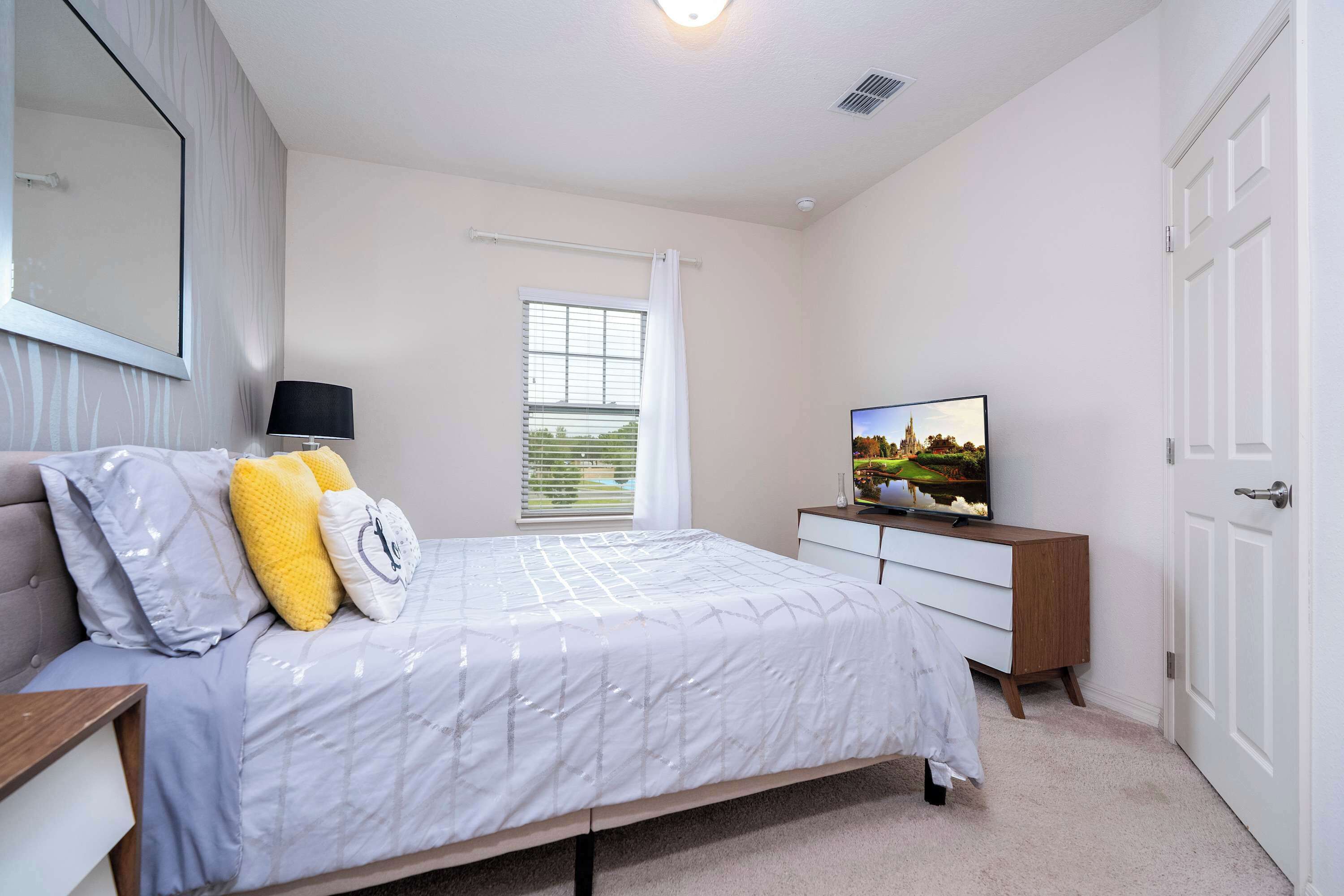 A bedroom with a bed, a dresser, a TV, and a window with curtains.