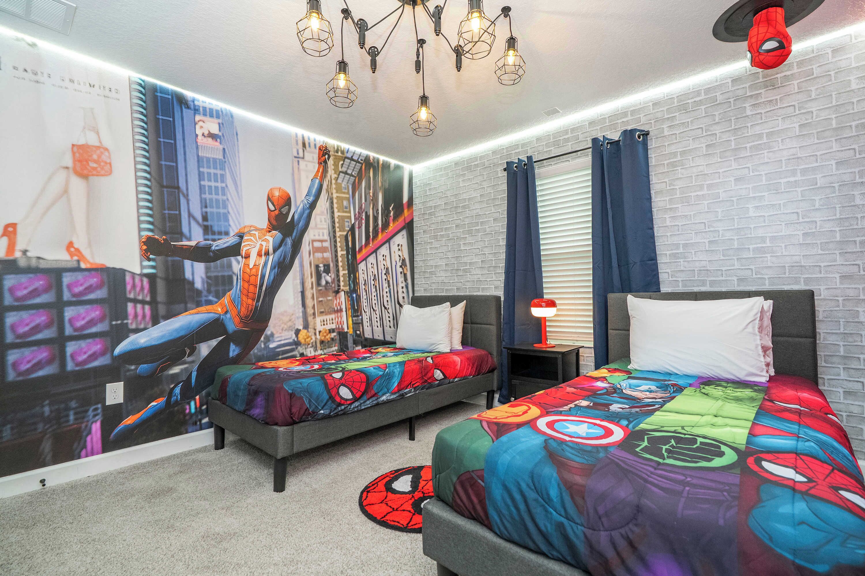 Una camera da letto con due letti, ognuno con copripiumino a tema Spider-Man, un murale raffigurante Spider-Man sulla parete e un lampadario moderno.