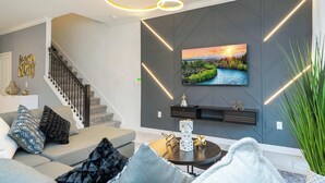 A modern living room with a gray sofa, a coffee table, and a TV mounted on the wall. - Stunning 4Bd W/ Pool @ Storey Lake 4239 (Kissimmee)