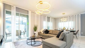 A modern living room with a sectional sofa, a coffee table, and a dining area with a table and chairs. - Stunning 4Bd W/ Pool @ Storey Lake 4239 (Kissimmee)