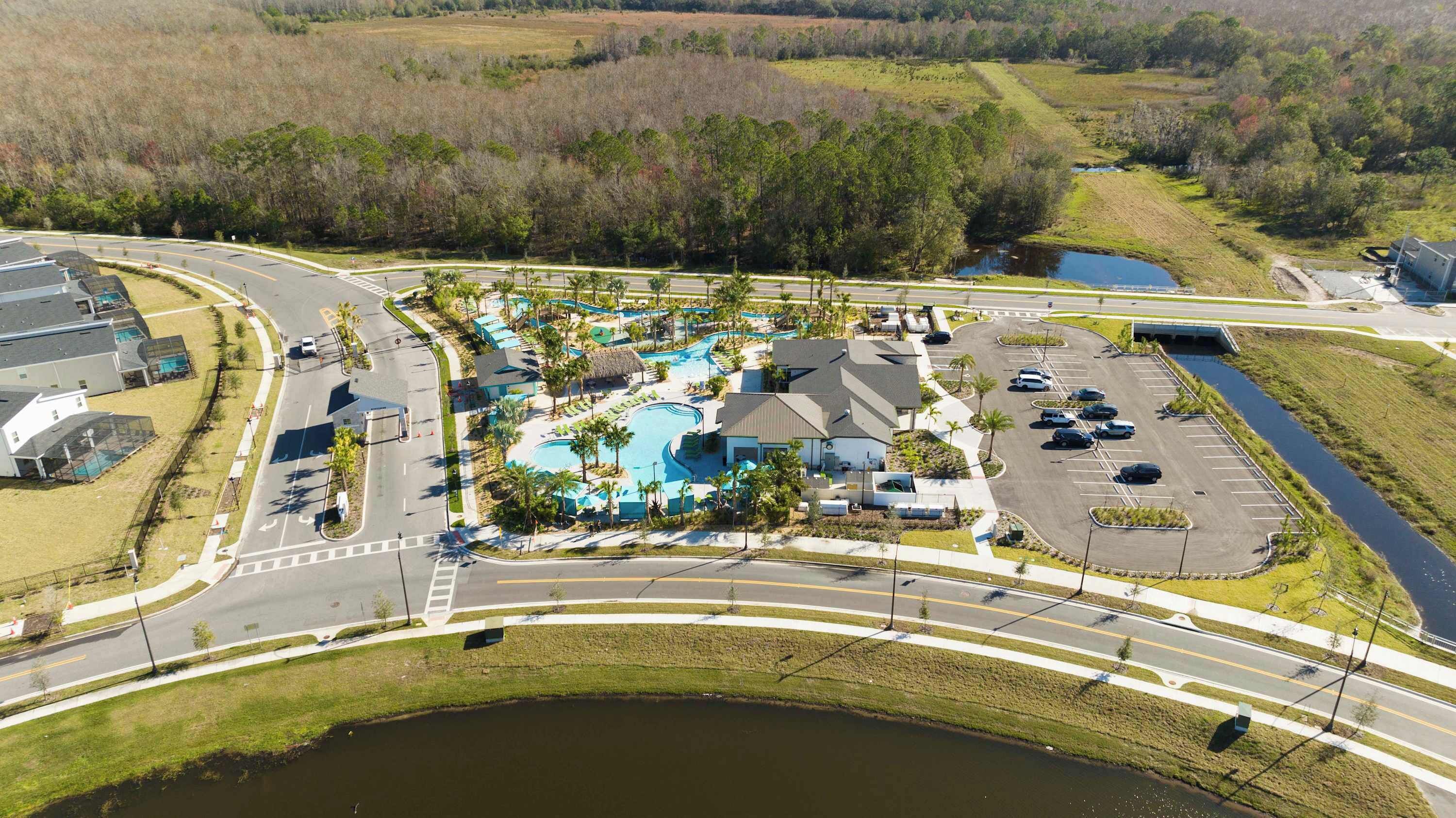 An aerial view of a resort with a swimming pool, parking area, and a road intersection.
