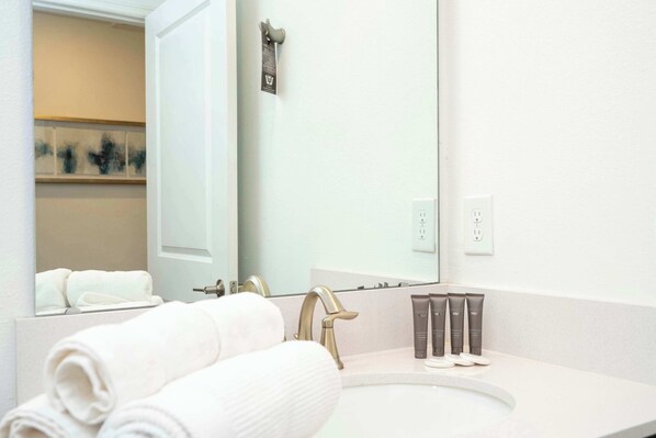 A modern bathroom with a white sink, gold faucet, and a large mirror. There are towels and toiletries on the counter. - Stunning 4Bd W/ Pool @ Storey Lake 4239 (Kissimmee)