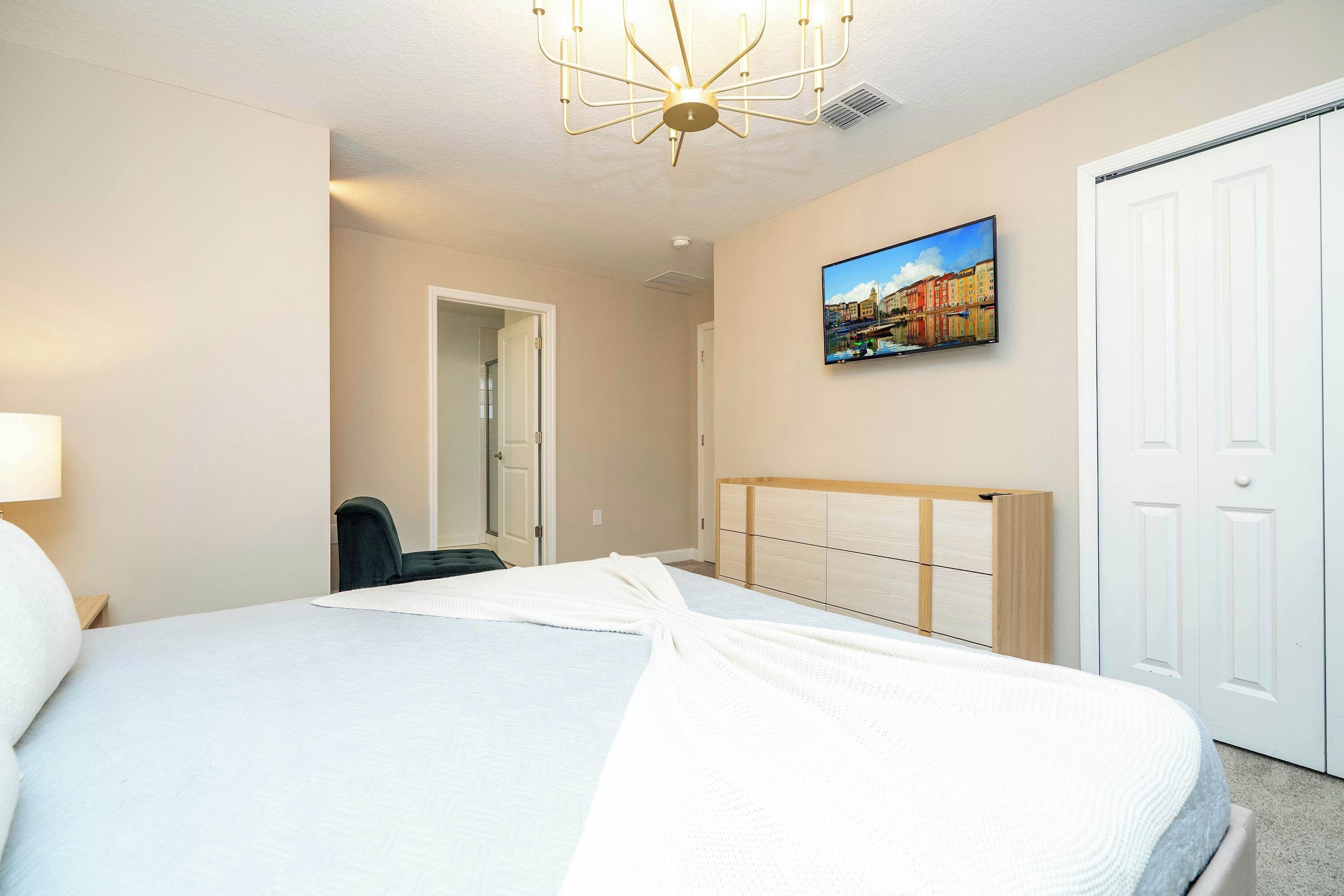 A hotel room with a bed, a desk, a chair, a television on the wall, and a door.