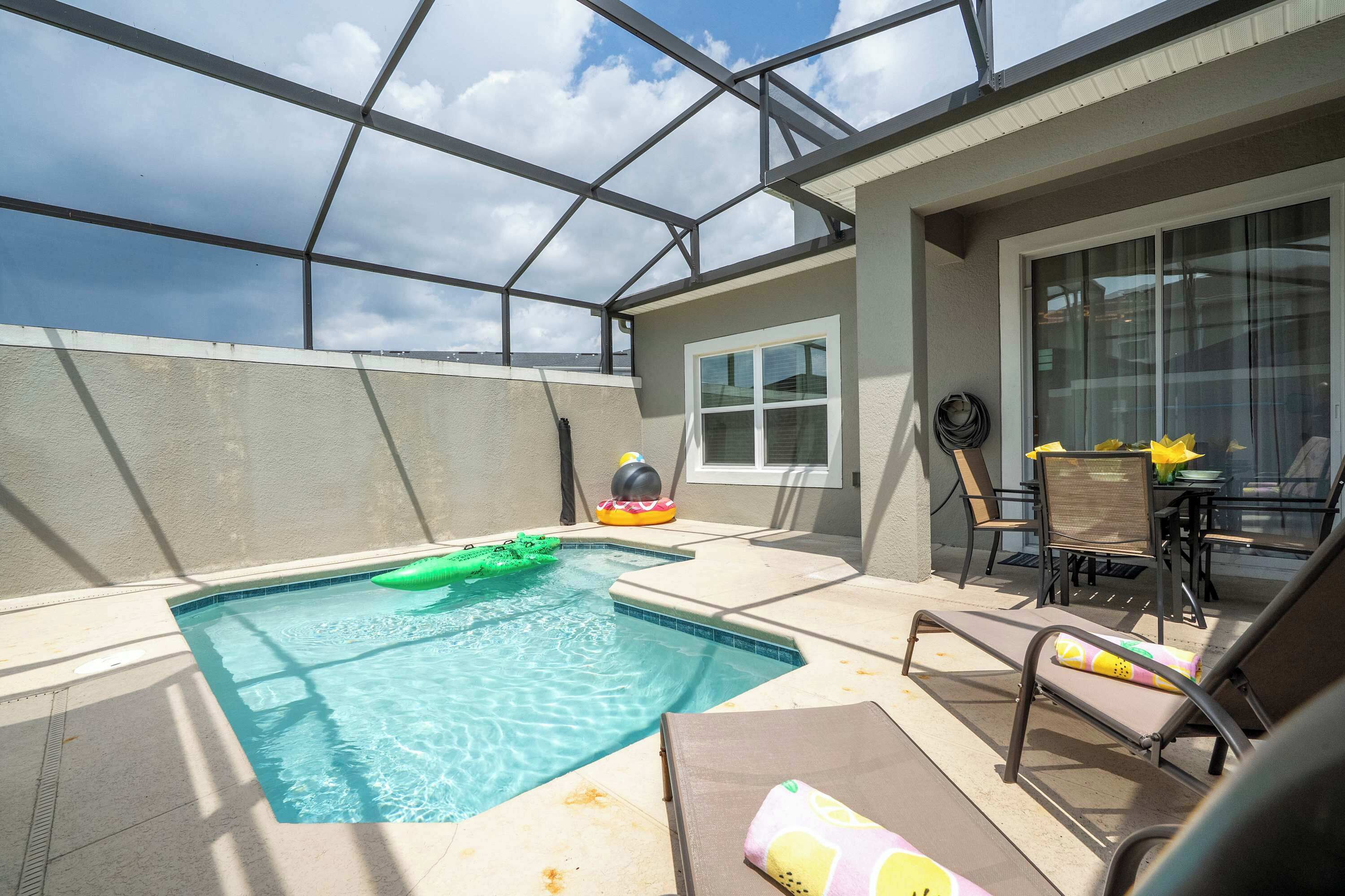 A rooftop pool with a glass enclosure, lounge chairs, and a table with yellow flowers.