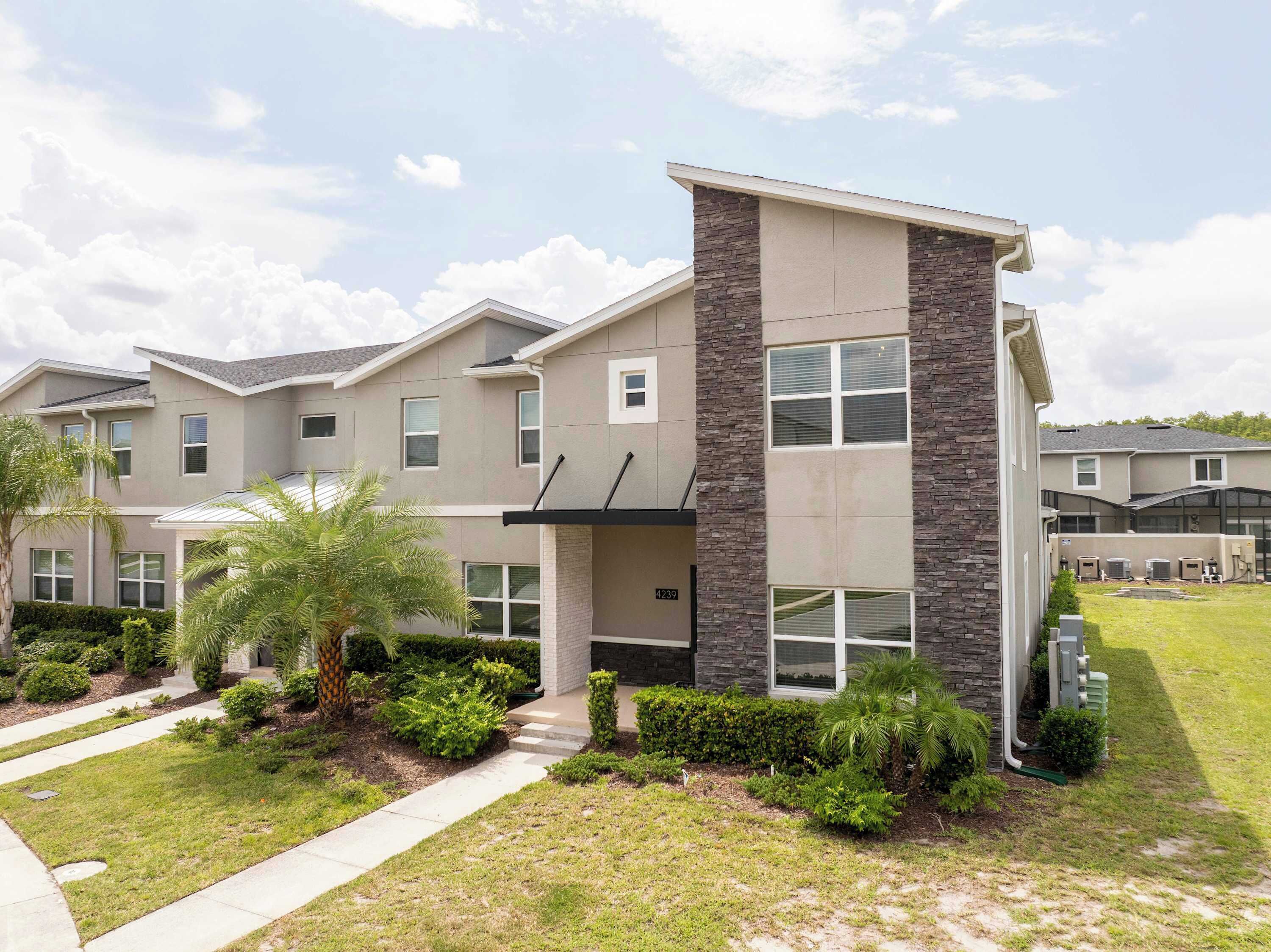 A modern multi-story residential building with a stone accent wall, multiple windows, and a well-maintained front yard with landscaping.