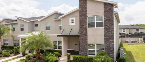 A modern multi-story residential building with a stone accent wall, multiple windows, and a well-maintained front yard with landscaping.