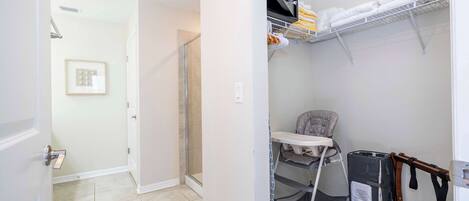 Habitación con ducha, una puerta blanca, un cuadro enmarcado, estante con toallas y un cochecito.