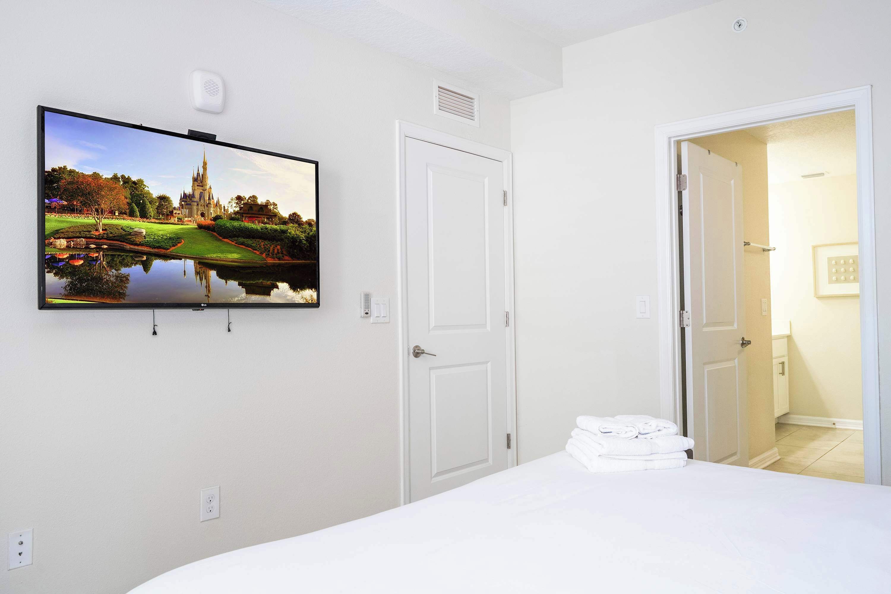 A hotel room with a bed, a flat-screen TV mounted on the wall, a door, and a bathroom visible through an open door.