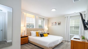 A bedroom with a bed, bedside tables, a desk, a TV, and a window with curtains. - Vibrant 5Br W/ Pool & Waterpark @Storey Lake 4811M (Kissimmee)