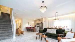 A modern living room with a staircase, a green sofa, a dining area, and a kitchen in the background. - Vibrant 5Br W/ Pool & Waterpark @Storey Lake 4811M (Kissimmee)
