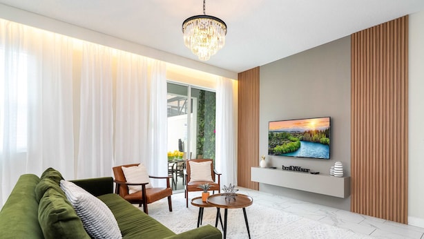 A modern living room with a green sofa, a wooden coffee table, and a flat-screen TV mounted on a wall. - Vibrant 5Br W/ Pool & Waterpark @Storey Lake 4811M (Kissimmee)