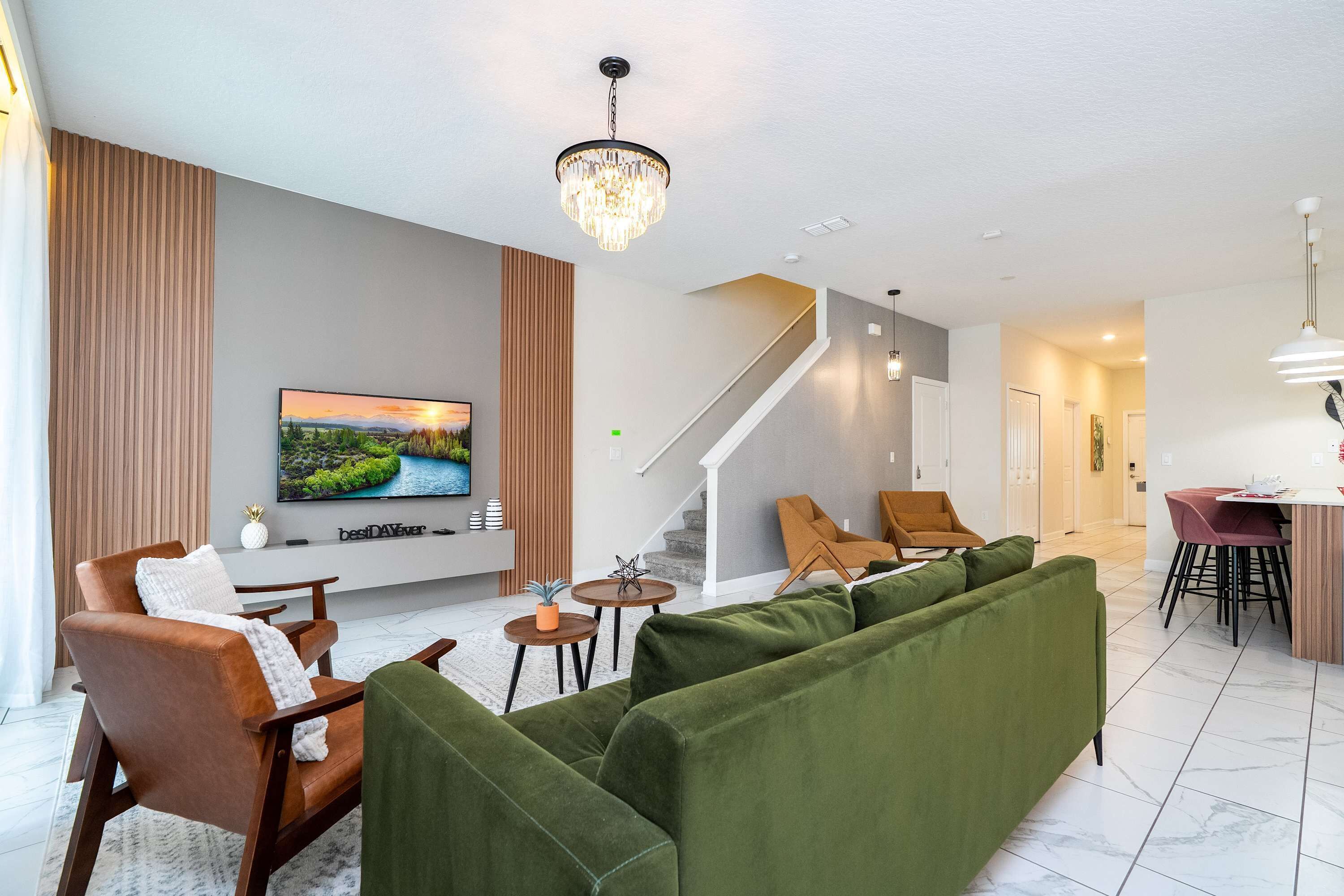A modern living room with a green sofa, a brown armchair, and a television on the wall.