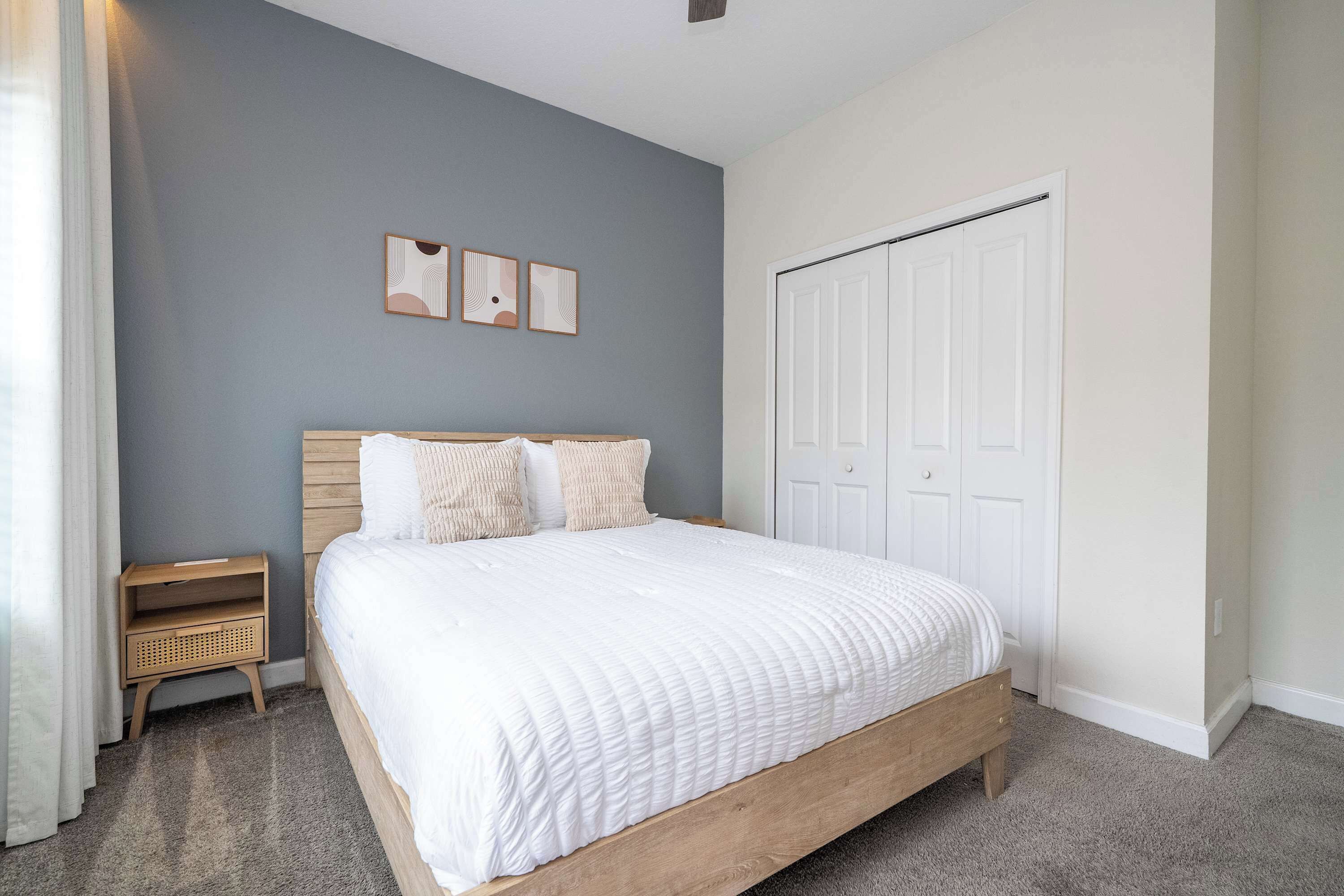 Une chambre à coucher avec un grand lit, une table de chevet, une armoire et trois tableaux accrochés au mur.