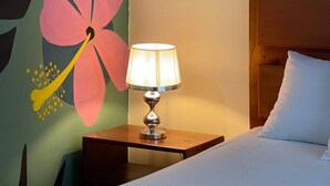 A hotel room with a bed, a nightstand with a lamp, and a wall with a floral mural.