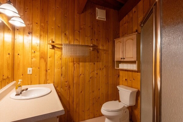 A wooden-paneled bathroom with a white sink, a toilet, and a cabinet above the toilet.