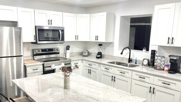 A modern kitchen with white cabinets, stainless steel appliances, a granite countertop, and bar stools. - Spacious House by TopGolf Pharr (Pharr)