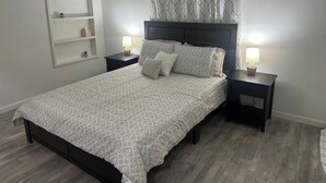 A neatly arranged bedroom with a bed, two bedside tables, a wall-mounted shelf, and a patterned curtain. - Spacious House by TopGolf Pharr (Pharr)