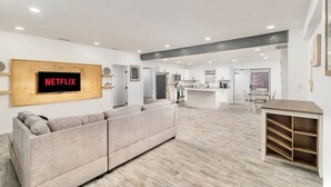 A modern living room with a sectional sofa, a kitchen area, and a dining space. - Spacious House by TopGolf Pharr (Pharr)