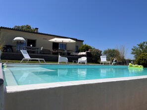 Ein Swimmingpool mit weißen Liegestühlen und eine Terrassenanlage mit Gartenmöbeln.