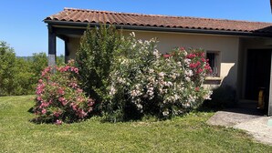 Ein Haus mit Ziegeldach, einer Laube und einem gepflegten Garten mit blühenden Sträuchern.