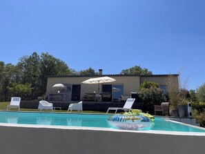 Una piscina con flotadores inflables, sillas de descanso blancas y una sombrilla.