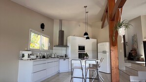 Eine moderne Küche mit weißen Schränken, einem Essbereich mit Tisch und Stühlen sowie einer hängenden Pflanze.