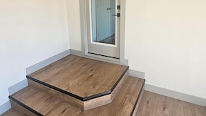 A room with a wooden floor, a door with a glass panel, and a small step leading to a door. - New carriage suite Calgary NW close to UofC (Calgary)