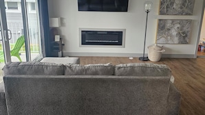 A living room with a gray sofa, a flat-screen TV mounted above a fireplace, and two abstract paintings on the wall. - New carriage suite Calgary NW close to UofC (Calgary)