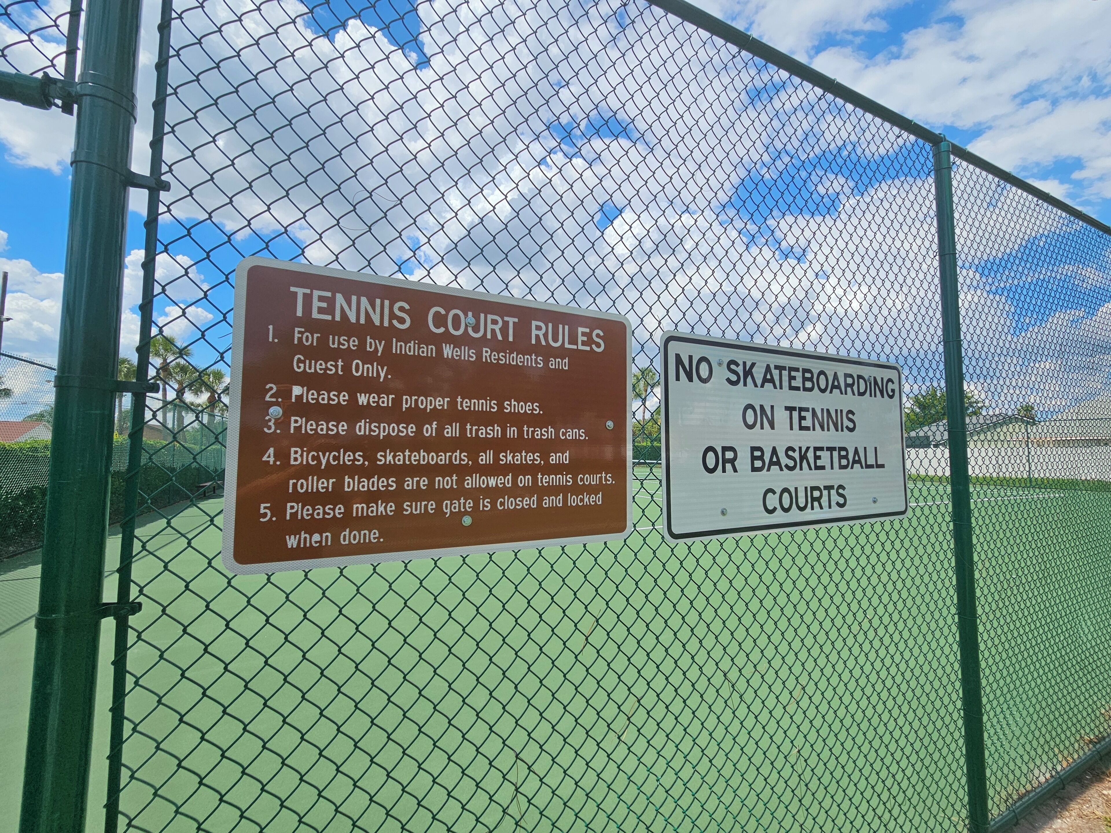 Una cancha de tenis con un cartel que enumera las reglas y un letrero que prohíbe patinar sobre ruedas y jugar al baloncesto.
