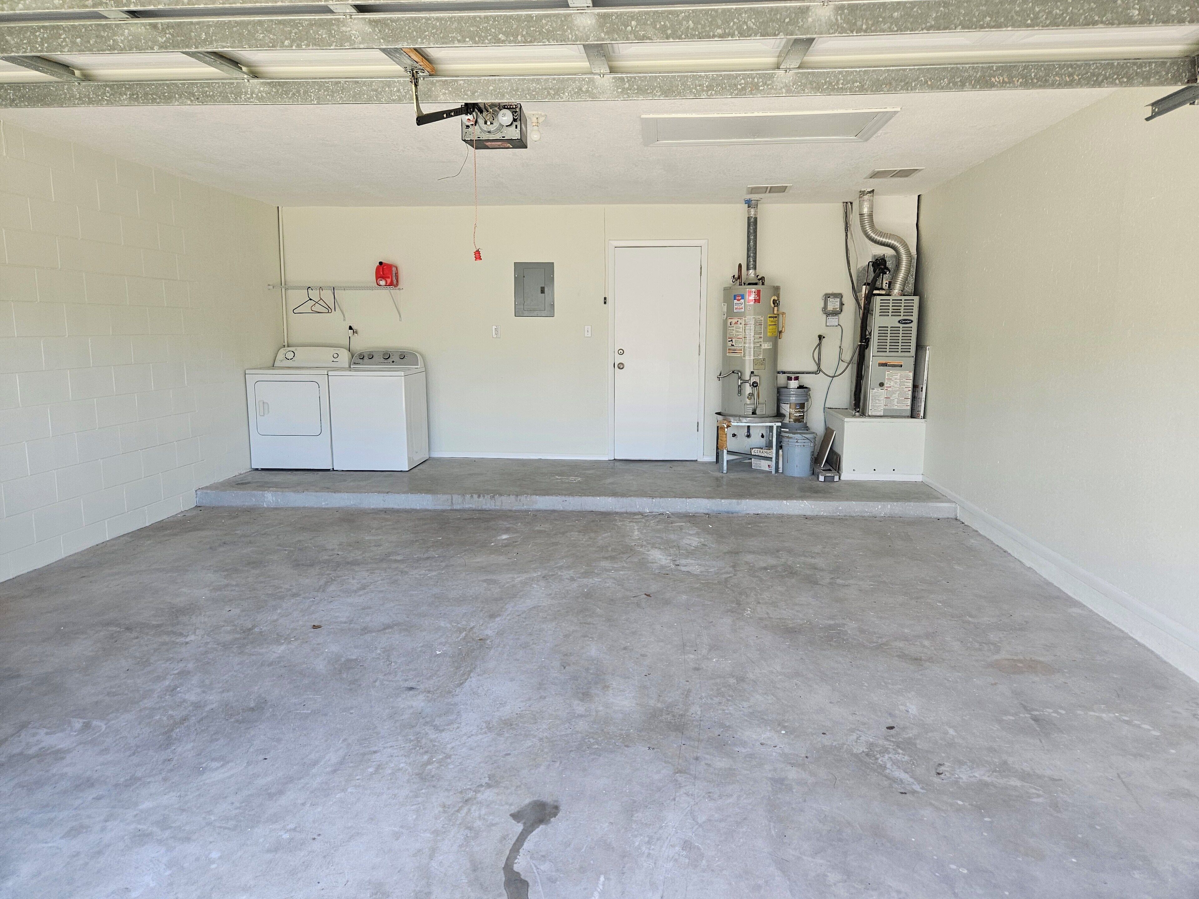 A garage with a washing machine, a door, and a utility room with equipment.